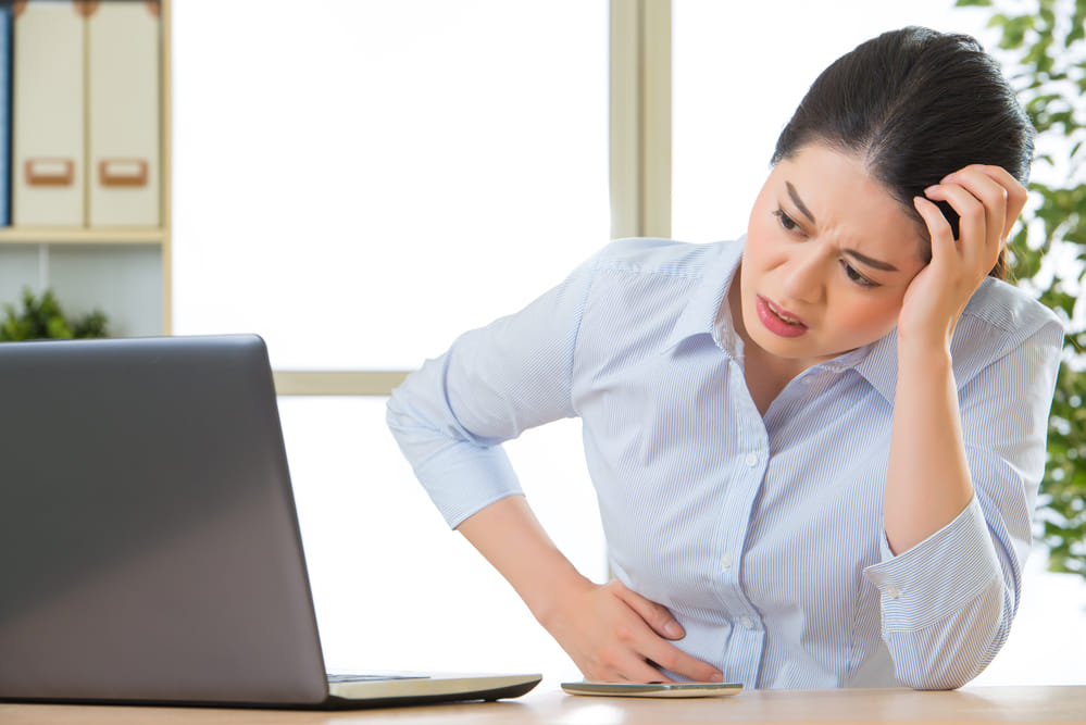 Young asian business woman with stomachache in office